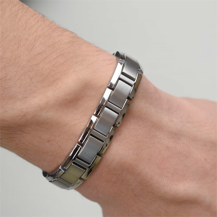 Een close-up toont de pols van een persoon die de Boccia Titanium Armband 0337-01 draagt, een stijlvolle zilveren titanium schakel herenarmband van Boccia, tegen een effen lichte achtergrond.