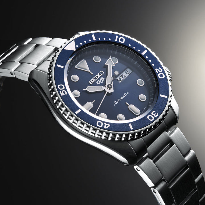Ontdek het verfijnde Seiko 5 Sports herenhorloge SRPD51K1 van Seiko, met een roestvrijstalen ontwerp met een blauwe bezel en wijzerplaat, lichtgevende uurmarkeringen, dag-datumweergaven en een automatisch uurwerk. De draaiende bezel met genummerde markeringen verbetert dit elegante uurwerk.