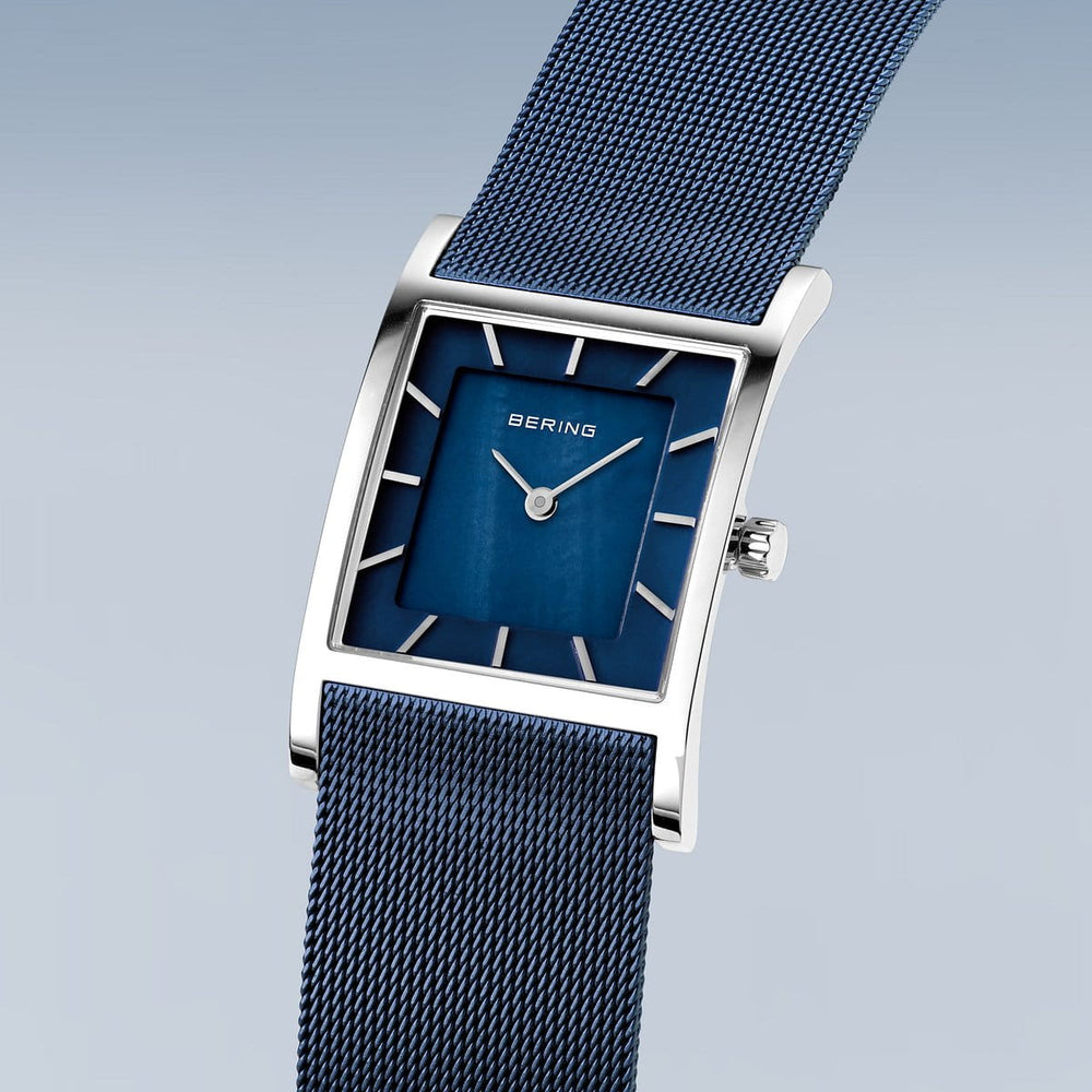 Het Bering Dameshorloge 10426-307-S heeft een strak, rechthoekig design met een blauwe wijzerplaat, zilveren uurmarkeringen en duurzaam Saffierglas. Het beschikt over een blauwe mesh band, zilveren kast met een kroon aan de rechterkant en een nauwkeurig Quartz uurwerk. Het merk Bering wordt elegant weergegeven op de wijzerplaat.