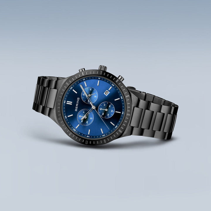 Het Bering-horloge 11743-727 is een stijlvol zwart polshorloge met een blauwe wijzerplaat met drie subwijzerplaten, een datumvenster, zilveren uurmarkeringen, een nauwkeurig Quartz-uurwerk en een metalen schakelband tegen een grijze achtergrond.