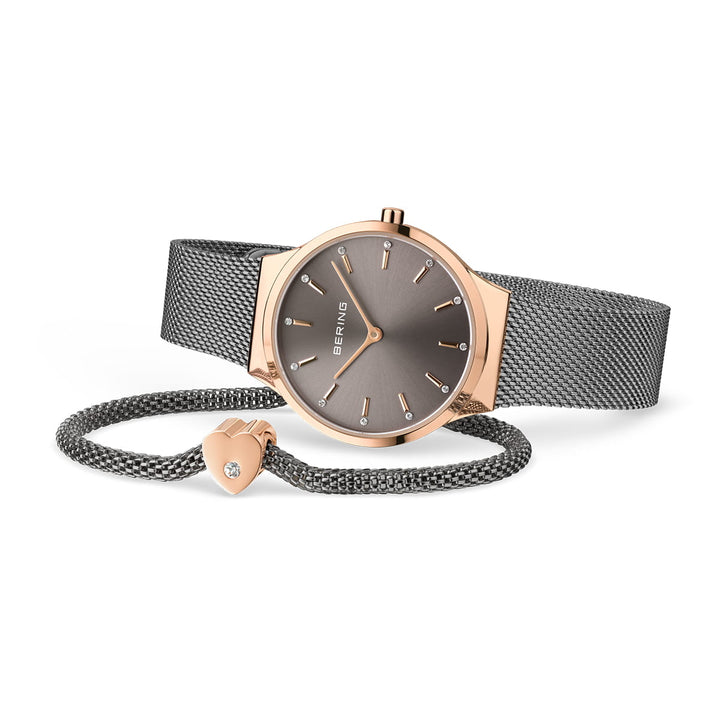 De Bering 12131-339-GWP is een chique quartzhorloge met een grijze Milanese band en roségouden kast, met een strakke grijze wijzerplaat met minimalistische gouden markeringen. Het wordt geleverd met een bijpassende armband met een hartvormige bedel versierd met een klein kristal.