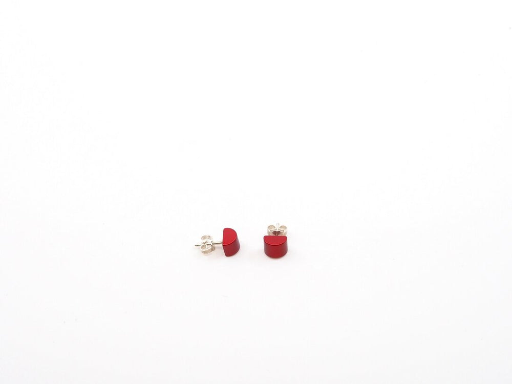 Een paar kleine, rode, halfronde oorknopjes van Otra Cosas Gekleurde half ronde oorbellen rood lijn, met moderne stijl met geanodiseerde aluminium achterkanten, weergegeven op een effen witte achtergrond.