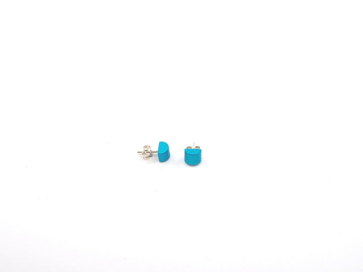 Een paar kleine, ronde turquoise oorbellen van Otra Cosa met de naam Gekleurde half ronde oorbellen turquoise zijn gemaakt van geanodiseerd aluminium met zilveren achterkanten, afgebeeld op een effen witte achtergrond.