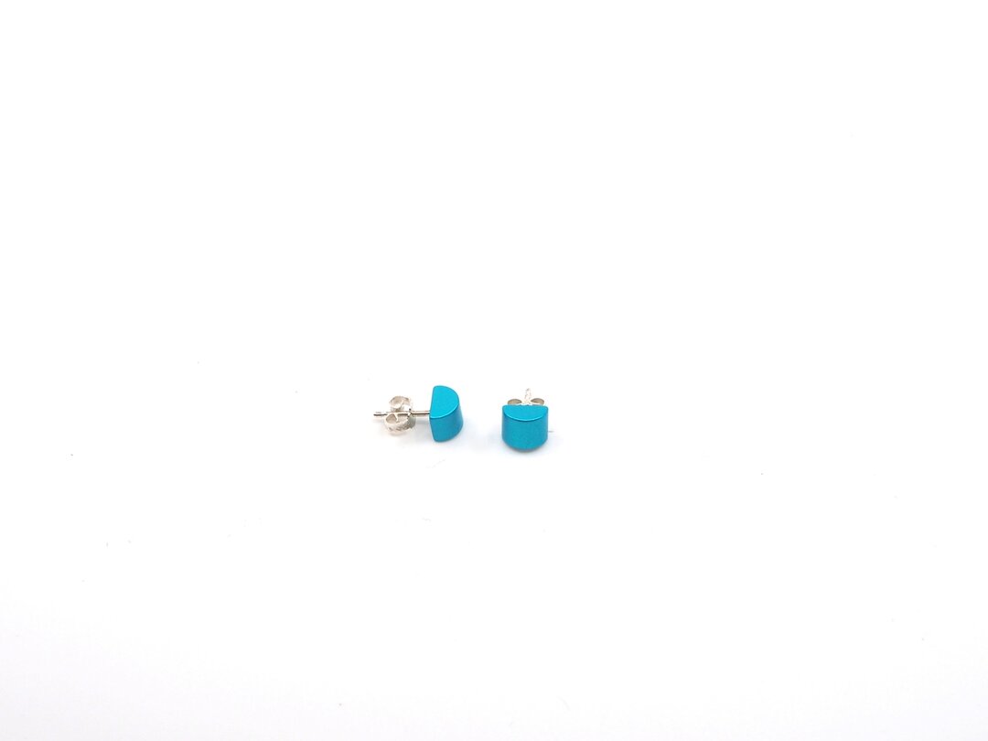 Twee turquoise Gekleurde kubus oorbellen van Otra Cosa, met zilveren achterkant, zijn geplaatst op een effen witte achtergrond.