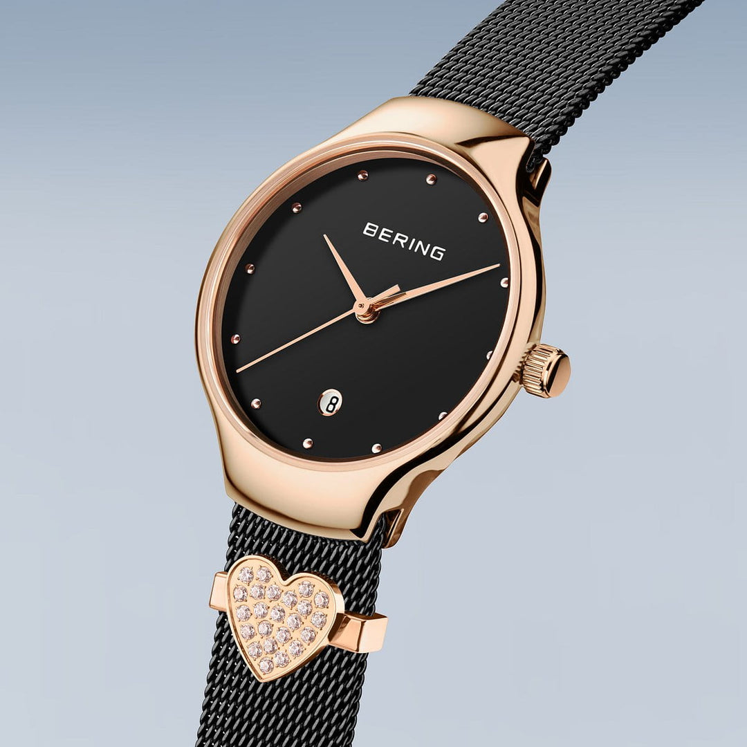 Het Bering 13326-262-GWP Dameshorloge heeft een zwarte ronde wijzerplaat, gouden roestvrijstalen kast en minimalistische puntvormige uurmarkeringen. Dit quartz-uurwerk omvat een getextureerde zwarte band met een met kristallen ingelegde hartbedel.