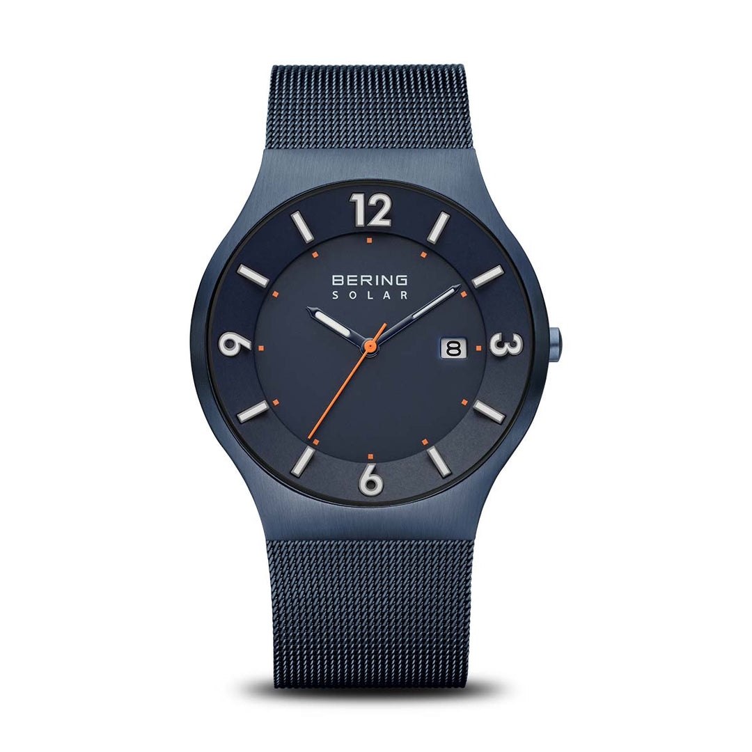 Het Bering 14440-393 solar polshorloge heeft een strakke donkerblauwe mesh band, zilveren cijfers en markeringen, een oranje secondewijzer en een datumweergave op 3 uur onder duurzaam saffierglas. Het merk Bering is zichtbaar onder de 12 uur positie.