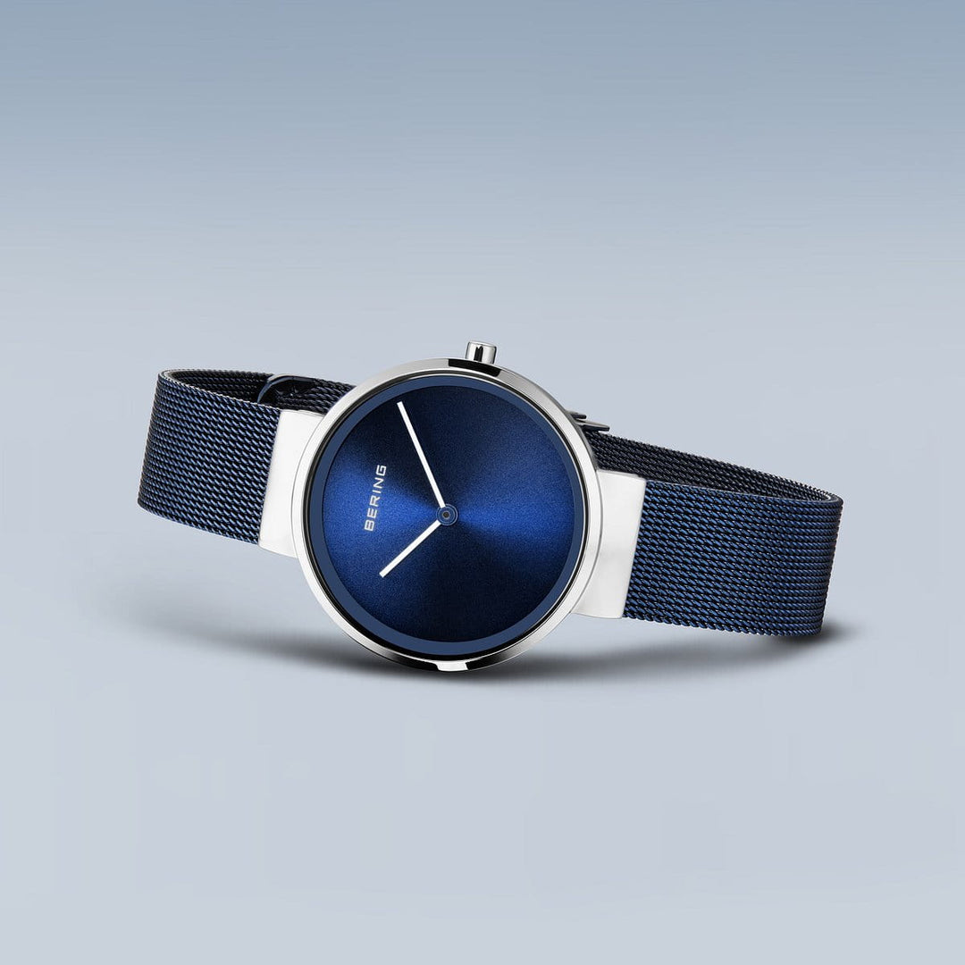 De Bering 14531-307 is een strak dameshorloge met een diepblauwe wijzerplaat en zilveren wijzers, wat een minimalistisch design laat zien. Gemaakt van roestvrij staal, heeft het een bijpassende blauwe meshband tegen een zachtgrijze achtergrond.