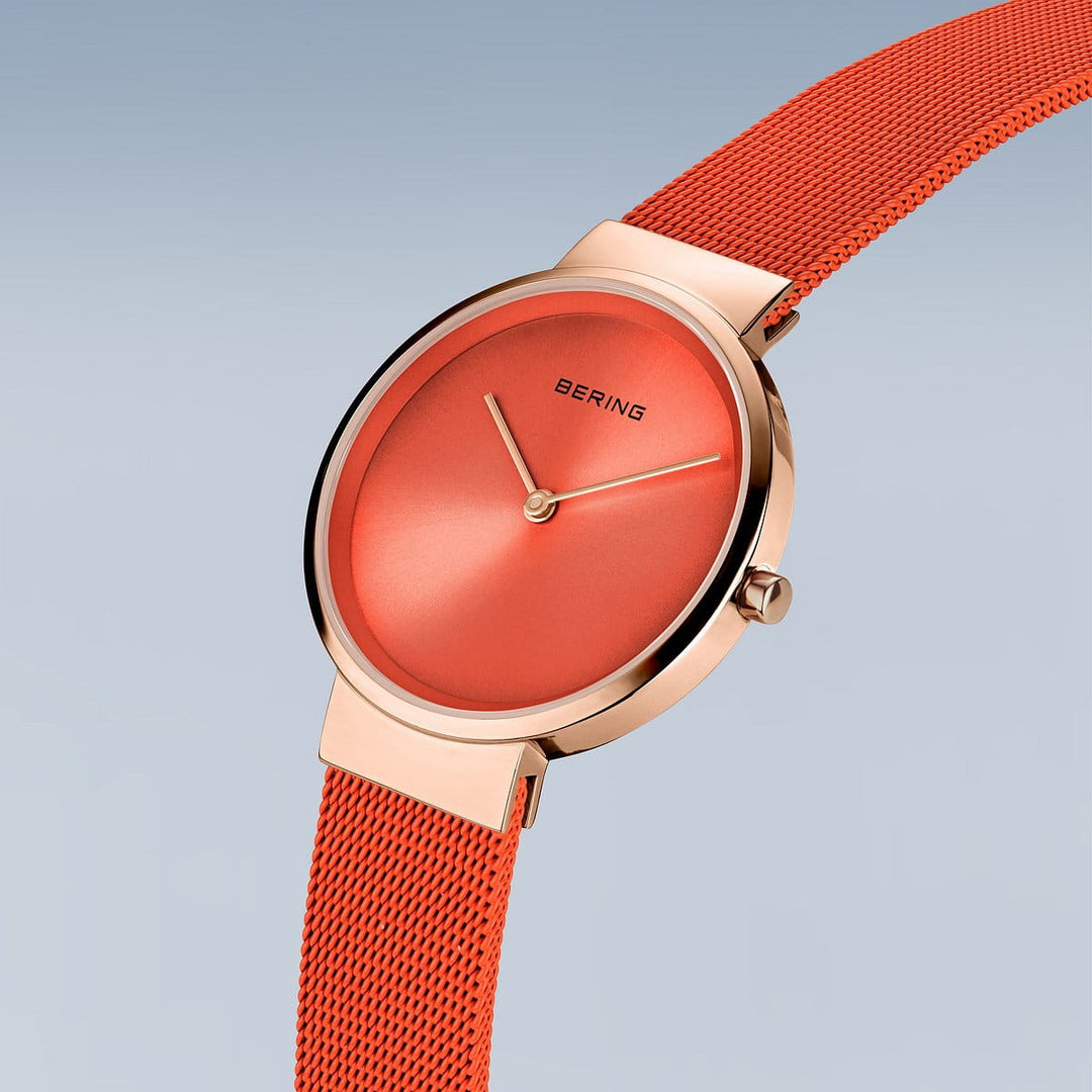 Ontdek Berings 14531-565: een minimalistisch oranje dameshorloge met een roségouden metalen kast en verstelbare mesh band. Het heeft bijpassende wijzers op een zachtblauwe tot lichtgrijze gradiënt wijzerplaat, nauwkeurig Quartz-uurwerk en duurzaam saffierglas.