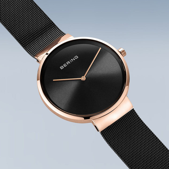 De Bering 14539-166 heeft een minimalistische zwarte wijzerplaat met roségouden accenten, een quartz-uurwerk en dunne roségouden wijzers tegen een lichtgrijze achtergrond, aangevuld met een strakke zwarte mesh-band.