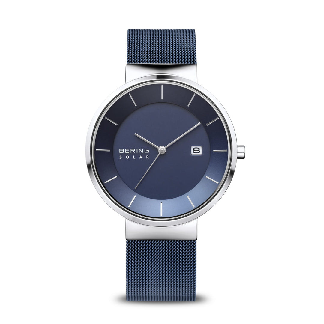 Het Bering 14639-307 Herenhorloge heeft een strakke blauwe wijzerplaat met zilveren kast, beschermd door Saffierglas. Het bevat minimale witte uurmarkeringen, een datumvenster op 3 uur, Bering Solar-branding en een blauwe meshband in een moderne, minimalistische stijl.