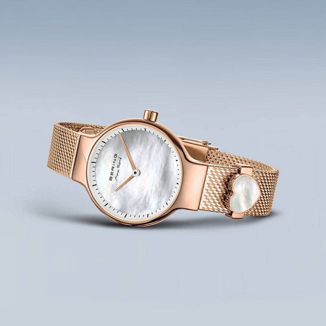Het Bering 15527-364-GWP dameshorloge in roségoud heeft een meshband, een ronde wijzerplaat met een witte parelmoeren wijzerplaat, zwarte uurmarkeringen en een quartz-uurwerk onder saffierglas, dat elegant afsteekt tegen een lichtgrijze achtergrond.