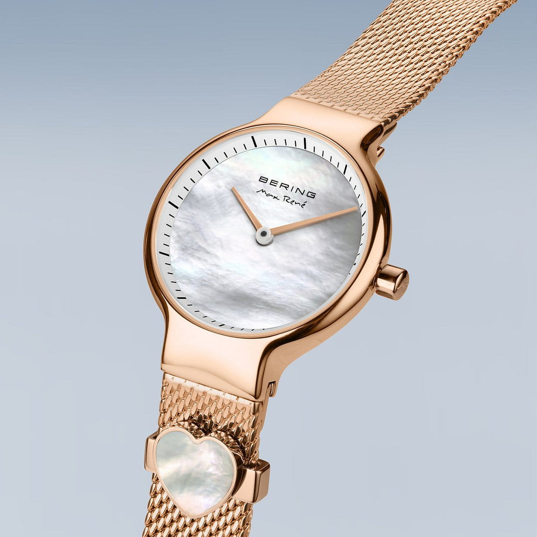 Het Bering horloge model 15527-364-GWP heeft een gouden mesh band, witte parelmoer wijzerplaat met zwarte wijzers en een hartvormig accent. Het heeft Saffierglas voor duurzaamheid en een elegante blauwgrijze gradiënt achtergrond.