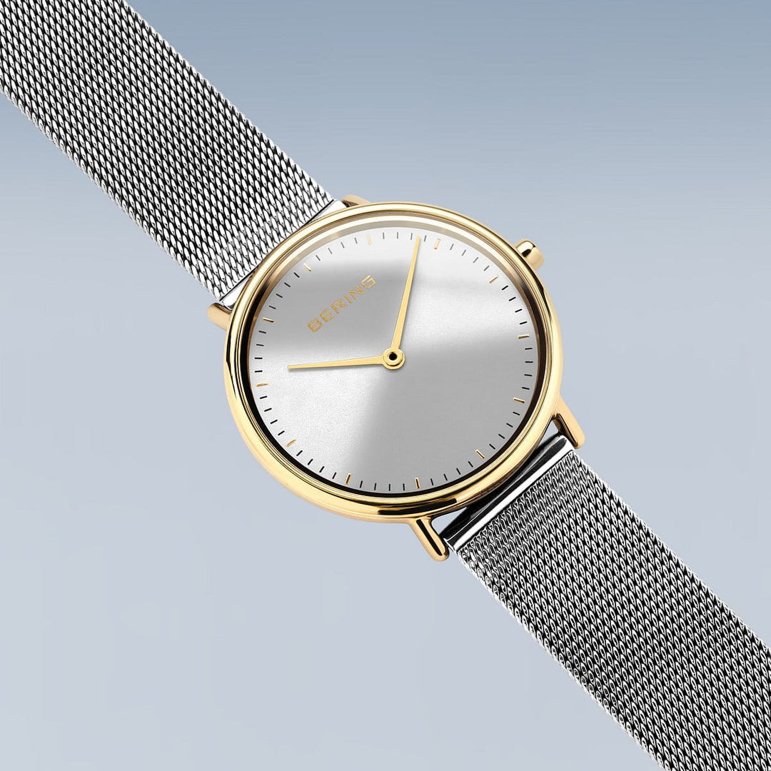 Het Bering 15729-010 dameshorloge straalt elegantie uit met zijn minimalistische design, met een ronde witte wijzerplaat versierd met gouden accenten, strakke uur- en minutenwijzers en een stijlvolle meshband. De merknaam wordt elegant weergegeven op de wijzerplaat tegen een gradiëntblauwe achtergrond in een roestvrijstalen kast.