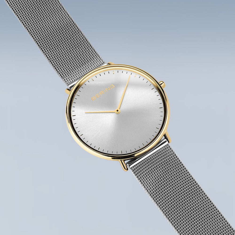 De Bering 15739-010 is een minimalistisch dameshorloge met een strakke, met goud omrande, roestvrijstalen kast met een meshband. De eenvoudige uurmarkeringen en twee wijzers op een effen zilveren wijzerplaat tegen een lichtblauwe achtergrond belichamen tijdloze elegantie.