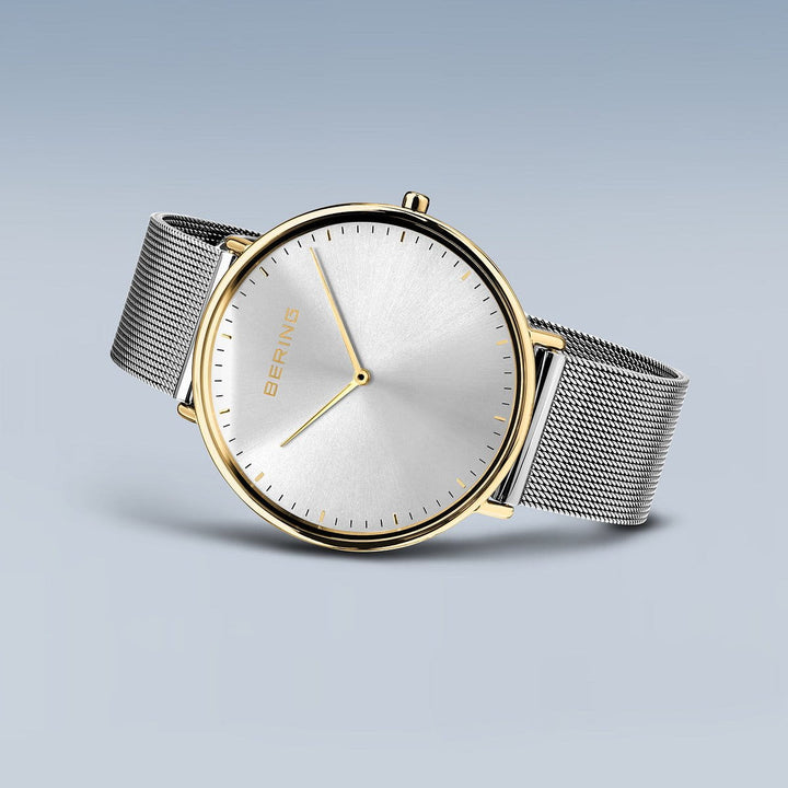 Het Bering 15739-010 Dameshorloge straalt tijdloze elegantie uit met een minimalistisch design, zilveren meshband en ronde zilveren wijzerplaat met gouden accenten. De roestvrijstalen kast versterkt de charme tegen een lichtblauwe gradiëntachtergrond.