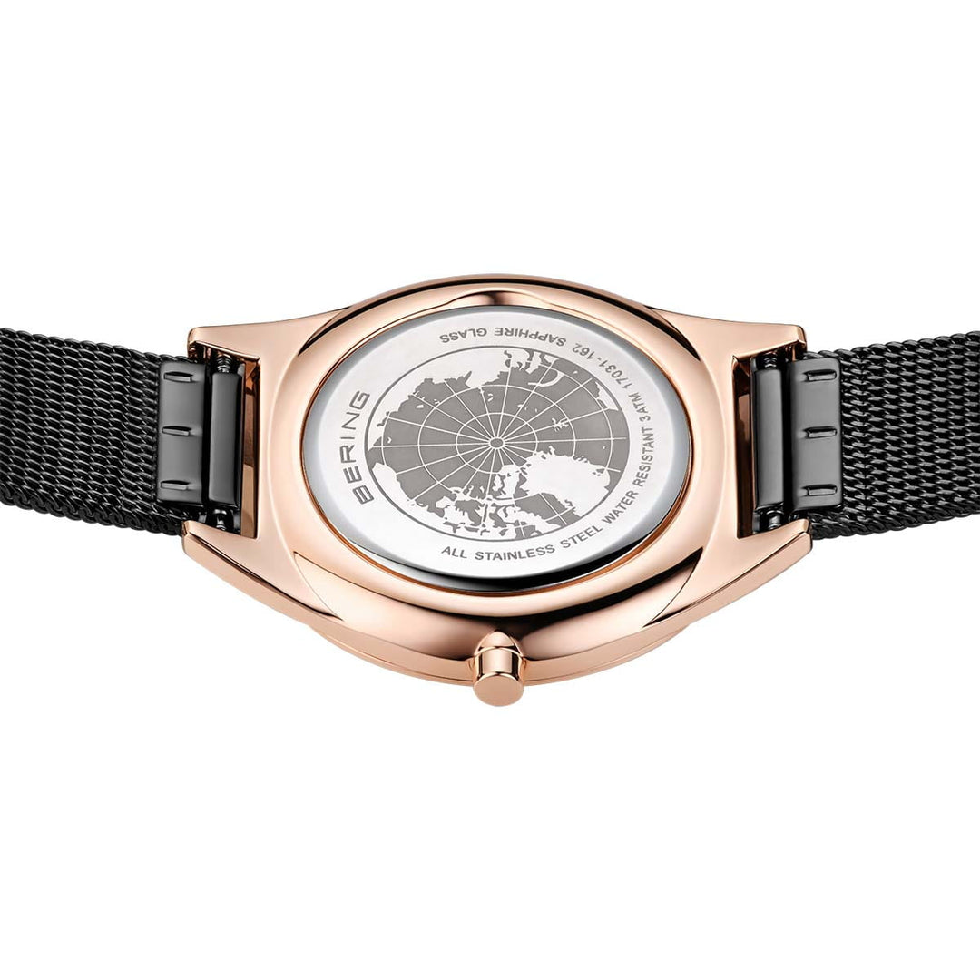 Het Bering model 17031-162 heeft een goudkleurige roestvrijstalen kast en een zwarte mesh band, met een geëtst wereldbolontwerp op de achterkant en inscripties die het duurzame roestvrij staal en krasbestendig saffierglas benadrukken.
