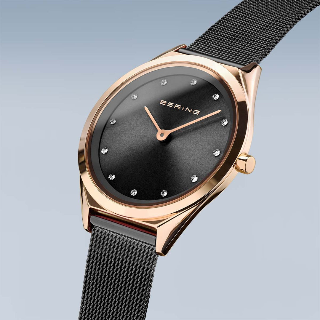 Unisex Bering quartz horloge 17031-162 heeft een zwarte wijzerplaat met minimalistische markeringen en kristallen uurindicatoren. De goudkleurige, roestvrijstalen kast combineert elegant met een zwarte meshband en krasbestendig saffierglas. BERING wordt prominent weergegeven tegen de lichtblauwe achtergrond.