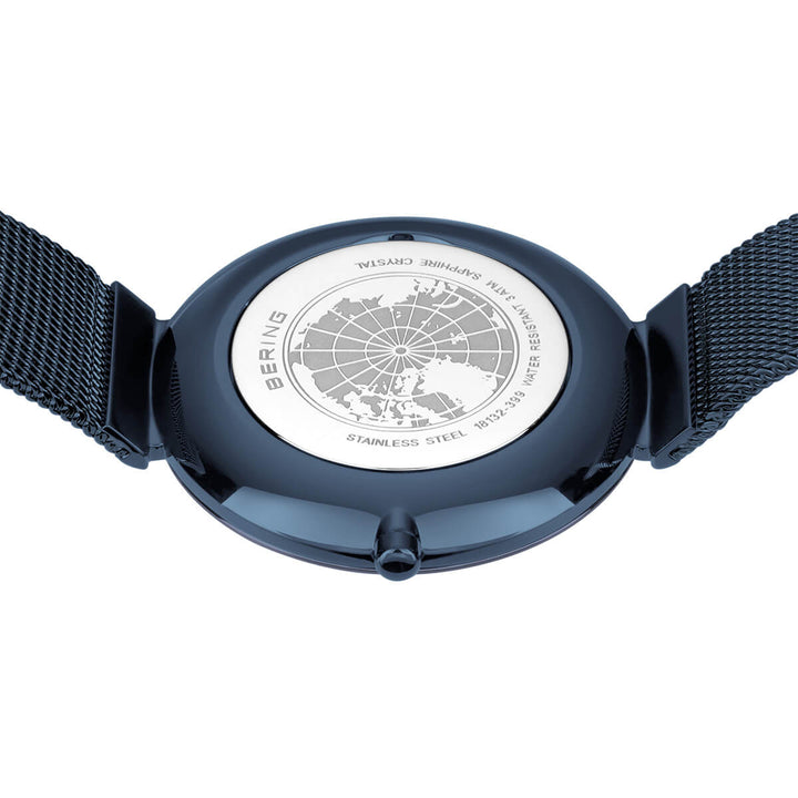 Een close-up van het bering dames horloge met blauwe wijzerplaat - 18132-399 toont een wereldkaartontwerp gegraveerd op de achterkant, met saffierglas, roestvrij staal, een Milanees-band en BERING rondom de kaart.