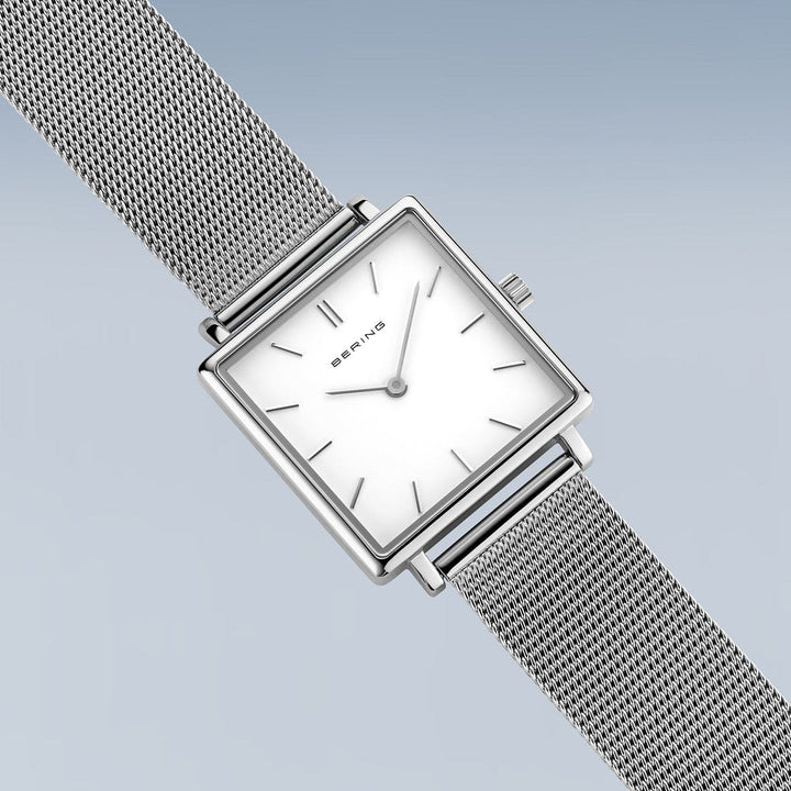 Het Bering dameshorloge 18226-004 heeft een vierkante wijzerplaat met minimalistisch design, quartz uurwerk, eenvoudige zilveren markeringen en wijzers op een witte wijzerplaat, een lichtblauwgrijze achtergrond met kleurverloop, een meshband van roestvrij staal en duurzaam saffierglas.