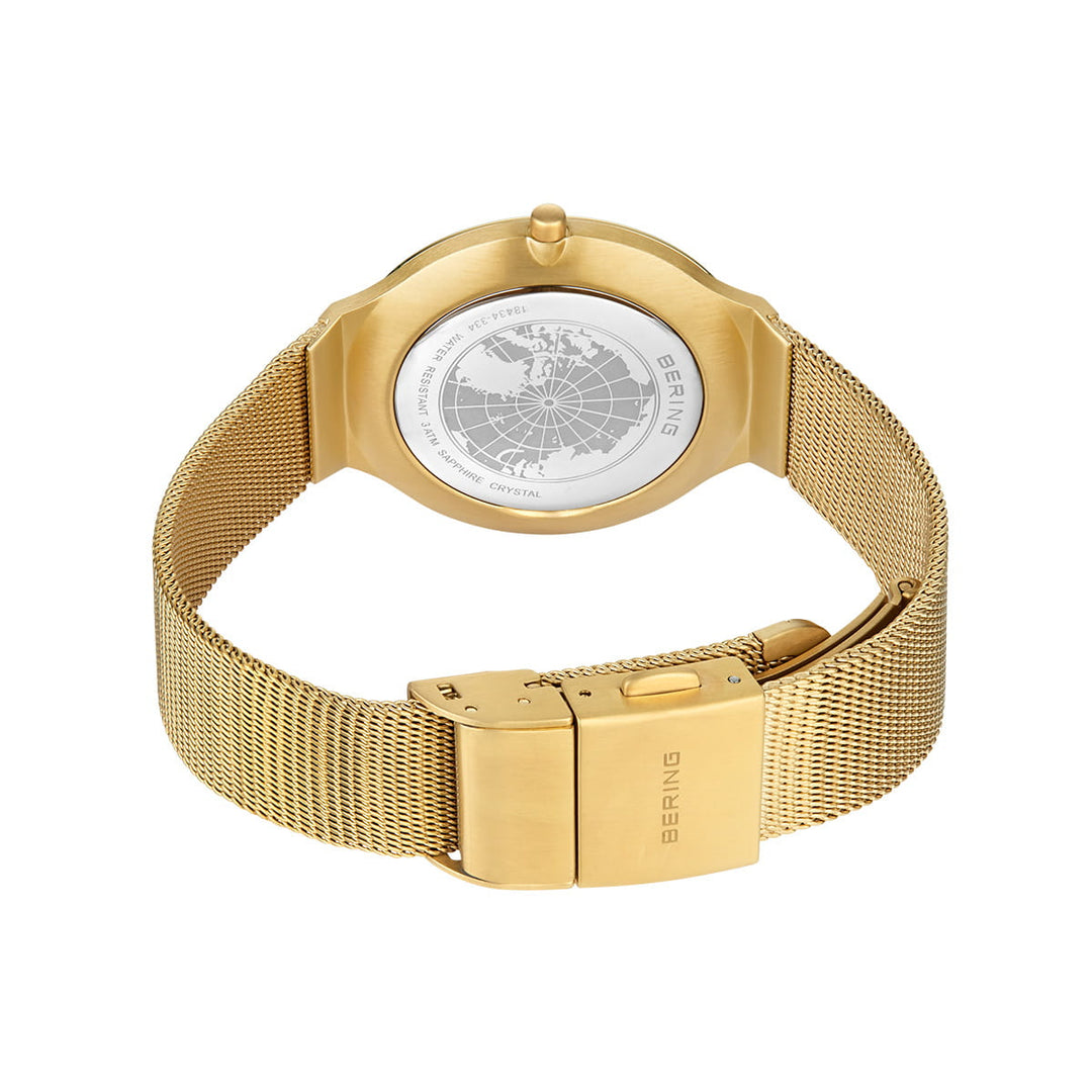 Het Bering dames horloge goud - 18434-334 pronkt met een gouden mesh band, een draaibare kompas bezel en een gegraveerde kaart op de achterkant. De merknaam, Bering, is zichtbaar op zowel de sluiting als de achterkant. Het wordt schuin weergegeven en toont het elegante ontwerp.