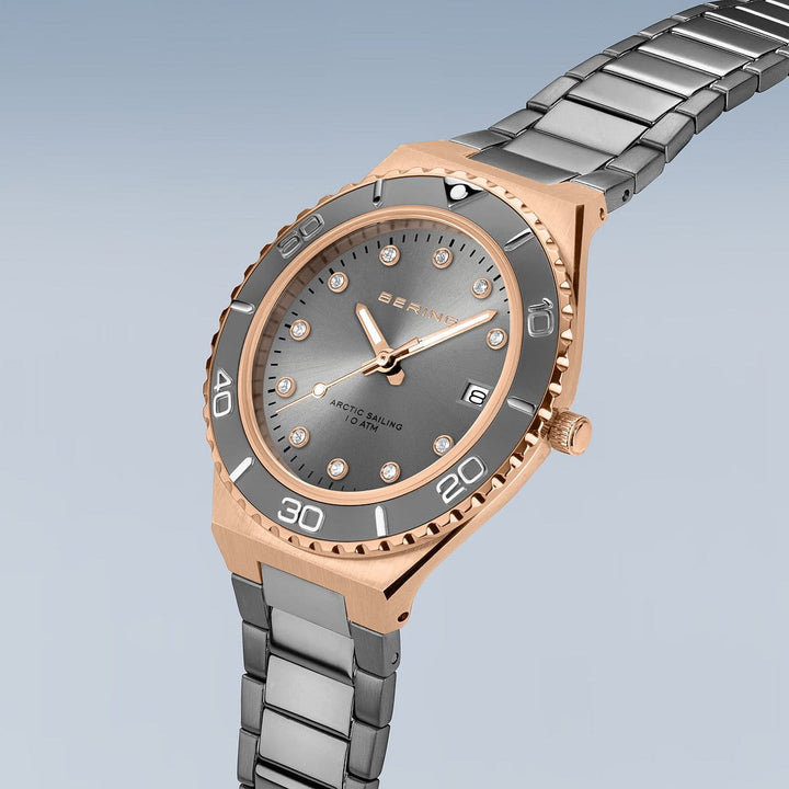 Een luxe Bering horloge, model 18936-769, heeft een zilveren en gouden roestvrijstalen kast en band. Het heeft een grijze wijzerplaat met kristallen uurmarkeringen, saffierglasbescherming, gouden wijzers en een grijze lunette. BERING en ARCTIC SAILING zijn elegant op de wijzerplaat gedrukt.
