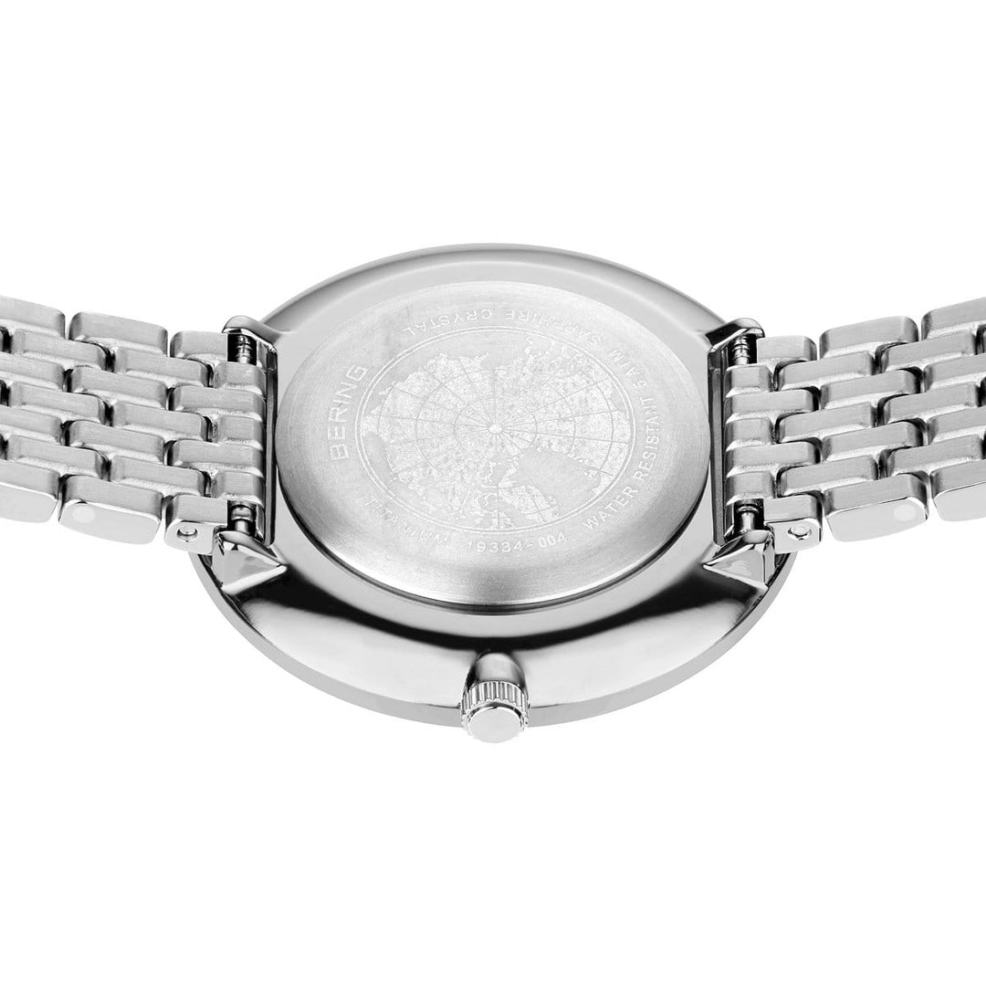 Close-up van een Bering dameshorloge met witte wijzerplaat - 19334-004, met een achterkant van titanium met een gegraveerd landkaartontwerp, minimalistische metalen band met glanzende afwerking, saffierglas en een kleine zijkroon.