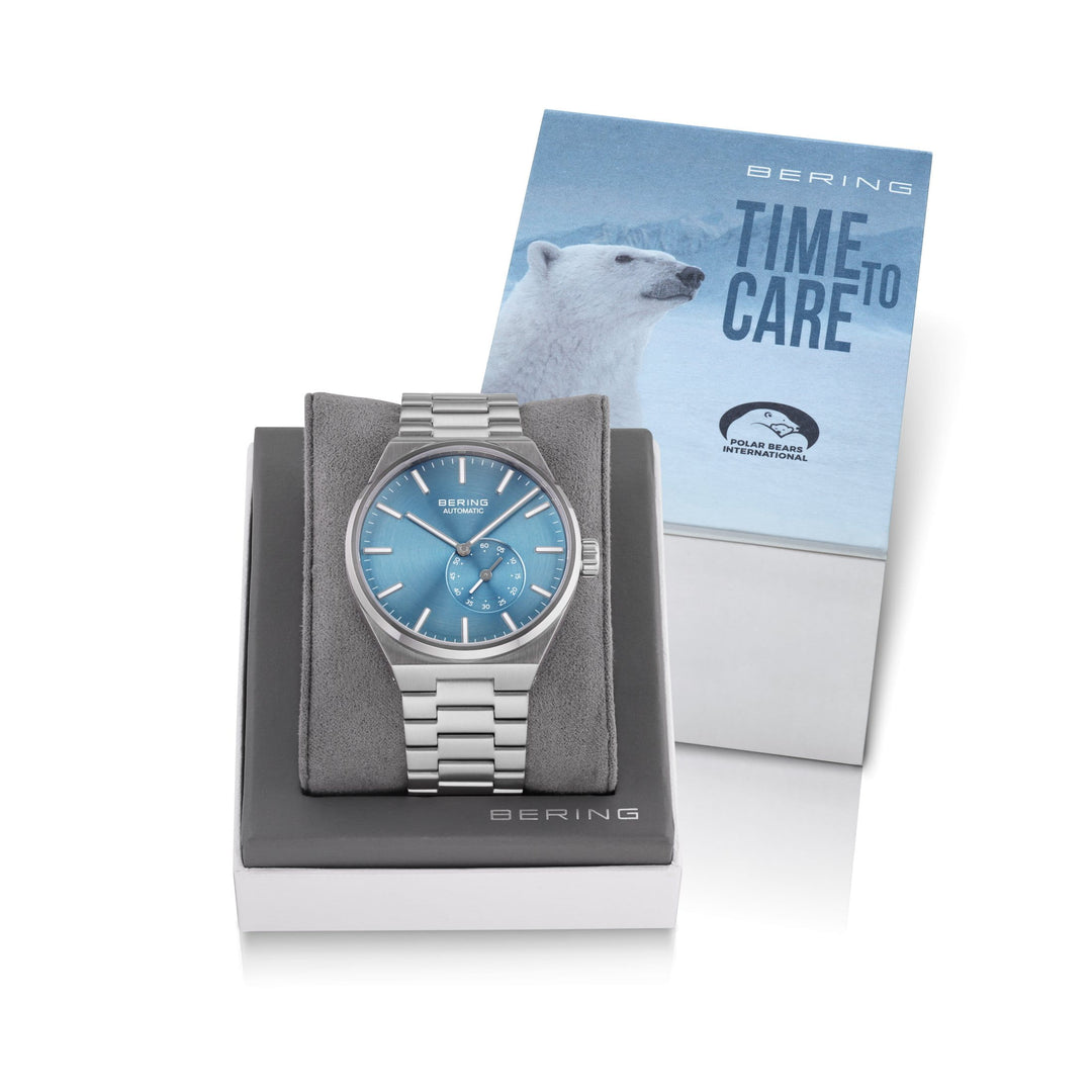 Het Bering herenhorloge 19441-Charity met een blauwe wijzerplaat en saffierglas wordt elegant tentoongesteld op een grijs kussen. Met automatisch uurwerk met een tweede wijzerplaat, staat het voor een Bering-doos met een ijsbeer en TIME TO CARE.
