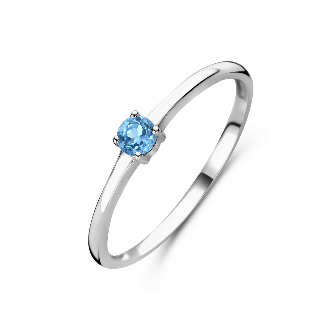De Van der Kooij Collectie ring met geboortesteen blauw topaas december is een gerhodineerde zilveren damesring met een dunne band en een ronde blauwe topaas in vierpoots zetting, getoond op een witte achtergrond.