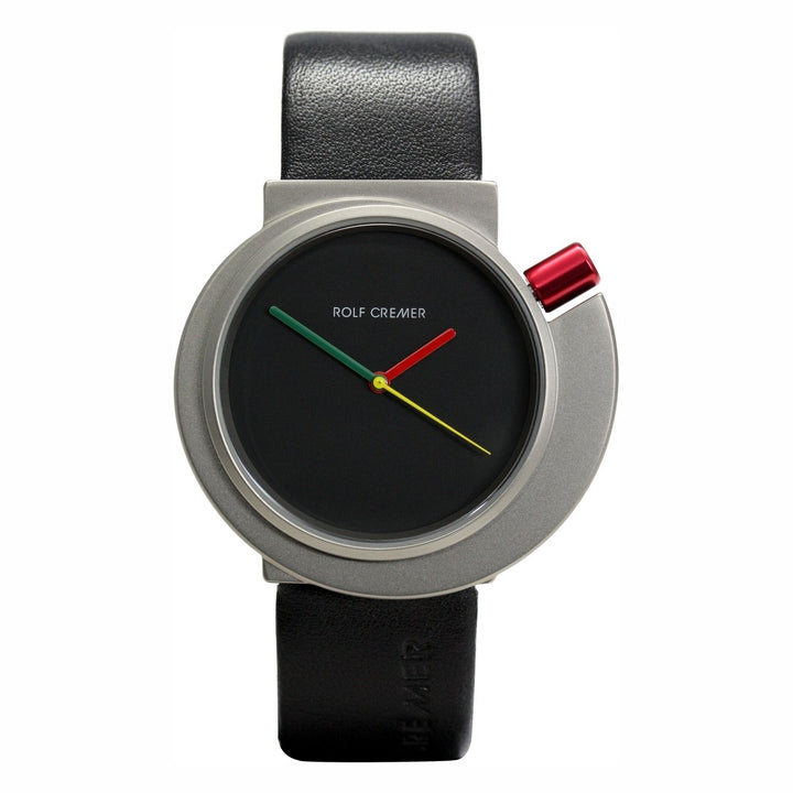 Het Rolf Cremer Horloge 492314 is een modern unisex quartz horloge met een ronde zwarte wijzerplaat, groene, rode en gele wijzers, een zilvergrijze kast met een rood accent en een zwarte leren band. Het Rolf Cremer logo verschijnt in het wit op de wijzerplaat.