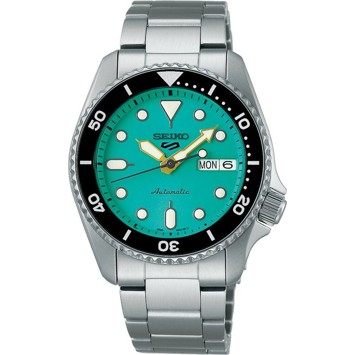 Het Seiko 5 Sports herenhorloge SRPK33K1 van Seiko heeft een turquoise wijzerplaat met witte uurmarkeringen, een dag-datumweergave met maandag en 6 en een zwarte lunette met minutenmarkeringen. Het biedt een automatisch uurwerk, waterdichtheid van 10ATM en combineert elegantie met functionaliteit op zijn zilveren metalen armband.