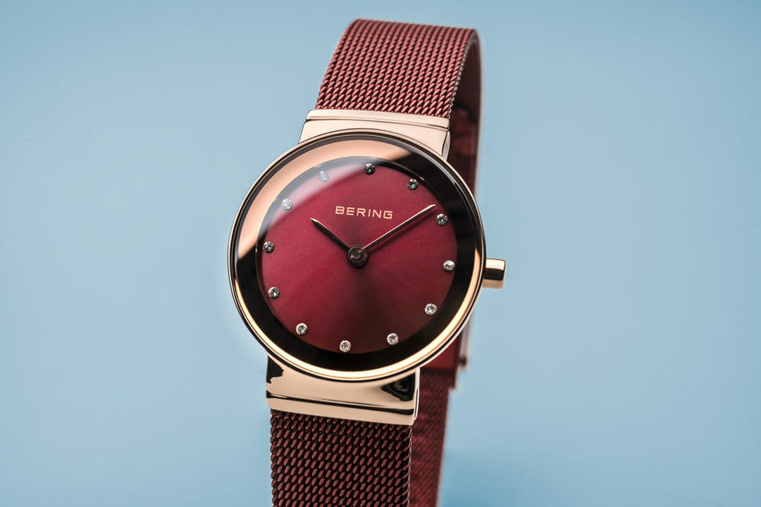 Close-up van het Bering Dameshorloge 10126-363 met een kast van roségoud, een kast van roségoud, een kast van mesh, minimalistische uurmarkeringen en een duurzaam quartz uurwerk van saffierglas tegen een lichtblauwe achtergrond.