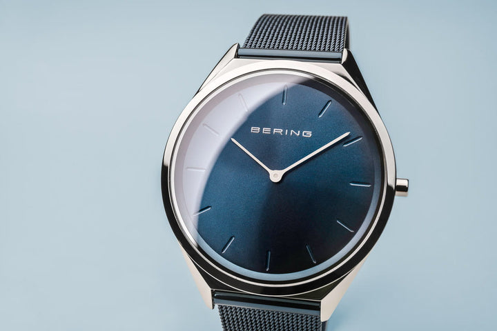 Hier ziet u het Bering unisex horloge 17039-307, met een gradiëntblauwe wijzerplaat, dunne zilverkleurige wijzers en saffierglas bescherming. De metalen kast is gecombineerd met een fijne mesh band, die allemaal opvallen tegen een lichtblauwe achtergrond.