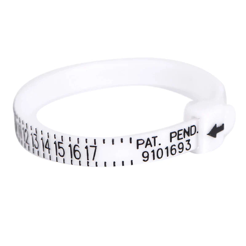 De Pas ring voor de perfecte ring maat van Juwelier van der Kooij is een witte, verstelbare ringmaatmeter van kunststof, met zwarte cijfers van 0-17, een kleine zwarte pijl en PAT. PEND. 9101693 bij de sluiting voor nauwkeurige metingen, elke keer weer.
