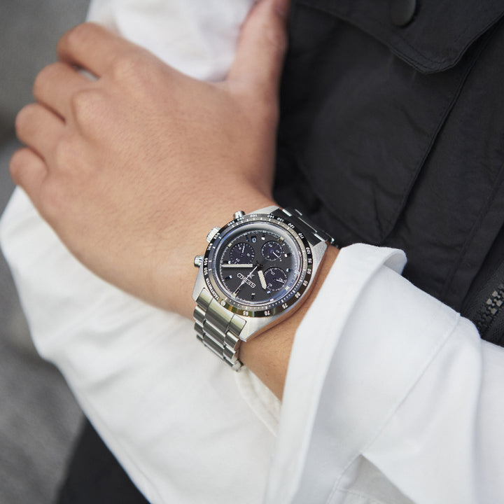 Een close-up toont een persoon die het Seiko Prospex heren horloge SSC819P1 draagt met een zwarte wijzerplaat en zilveren wijzers. De roestvrijstalen horlogekast zit op de linker pols over een witte mouw, terwijl ze de band met hun rechterhand verstellen.
