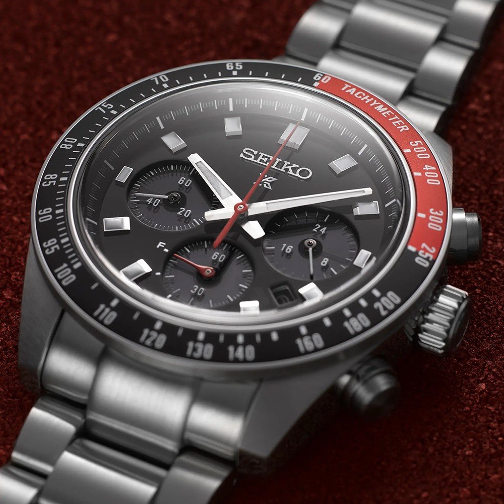 Close-up van de Seiko Prospex heren horloge SSC915P1 chronograaf in zilver op een rood oppervlak, met een zwarte wijzerplaat met drie subdials, zilveren markeringen en een secondewijzer met rode punt. De tachymeterschaal van de lunette is verdeeld in rood en zwart, wat de zonnetechnologie van Seiko benadrukt.