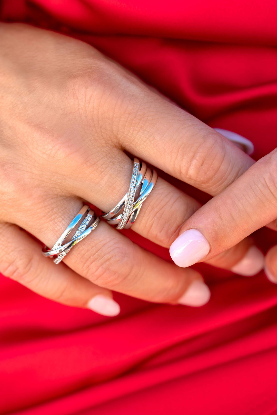 Een close-up van een hand met lichtroze nagels die zilveren ringen draagt, waaronder de Zinzi Ring zilver ZIR1790 van Zinzi-rustend op levendige rode stof.