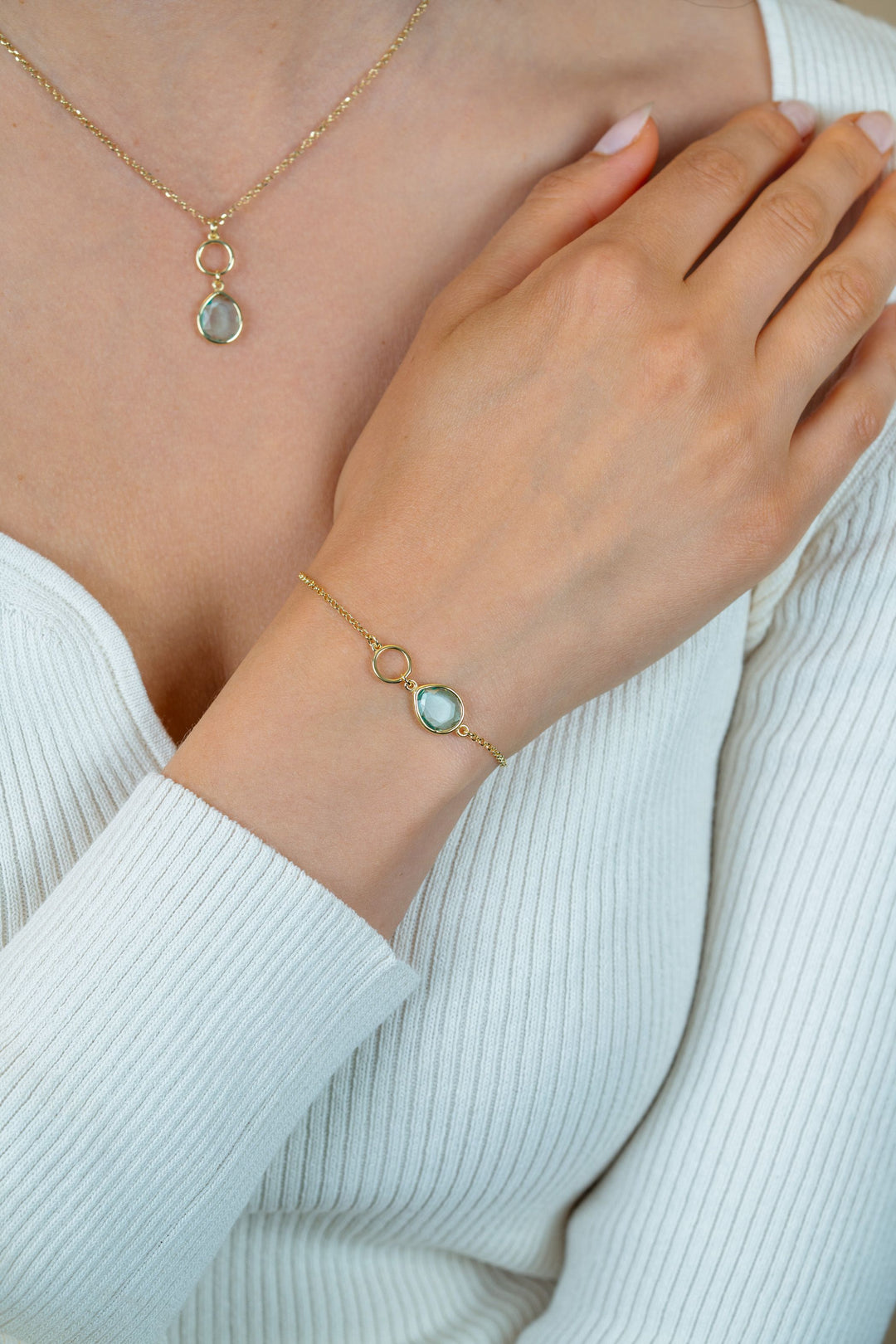 Een persoon met een wit geribbeld topje draagt een bijpassende gouden ketting en de Zinzi Armband verguld ZIA2716G van Zinzi, elk met een turquoise kleursteen in een delicaat gouden montuur. De armband rust zachtjes op de borst.