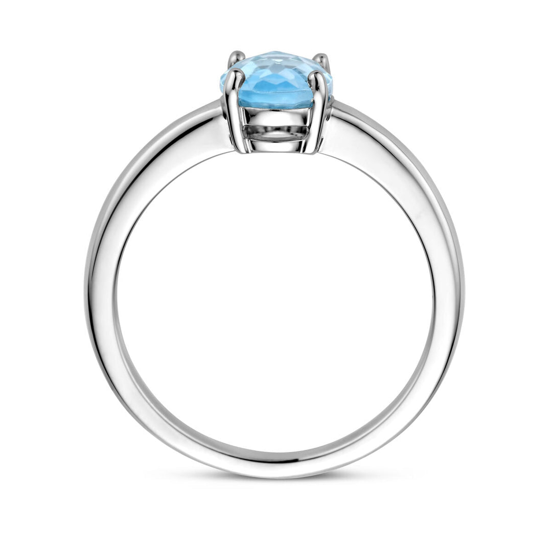 Een Van der Kooij Collectie ring blauw topaas zilver gerhodineerd met ronde, gefacetteerde blauwe topaas in een vierpoots zetting, zijaanzicht op witte achtergrond.