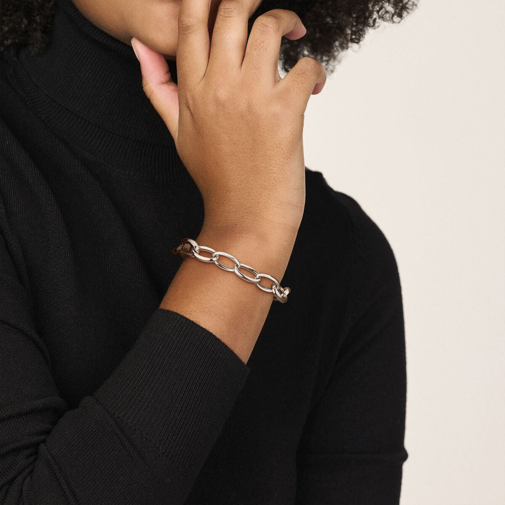 Een persoon in een zwarte coltrui laat zijn hand op zijn kin rusten, terwijl hij de Van der Kooij Collectie armband anker 10 mm 17 cm zilver gerhodineerd laat zien - een opvallende keuze voor fans van minimalistische sieraden.