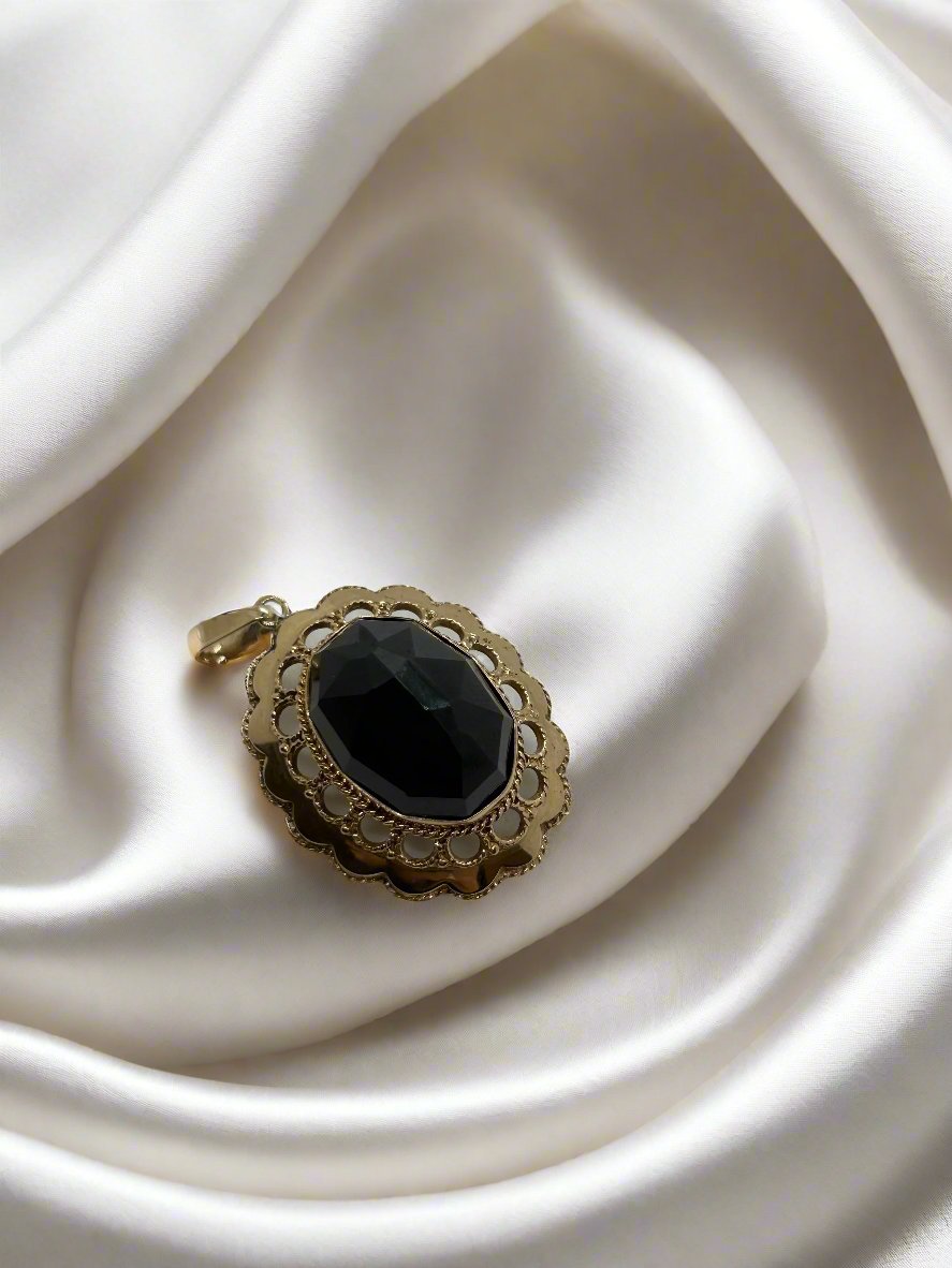De 14k vintage gouden Hanger van Juwelier van der Kooij heeft een grote granaat van 11g, elegant rustend op gladde witte zijden stof. Dit prachtige stuk heeft ingewikkelde details rond de edelsteen, wat verfijning en luxe toevoegt aan de scène.