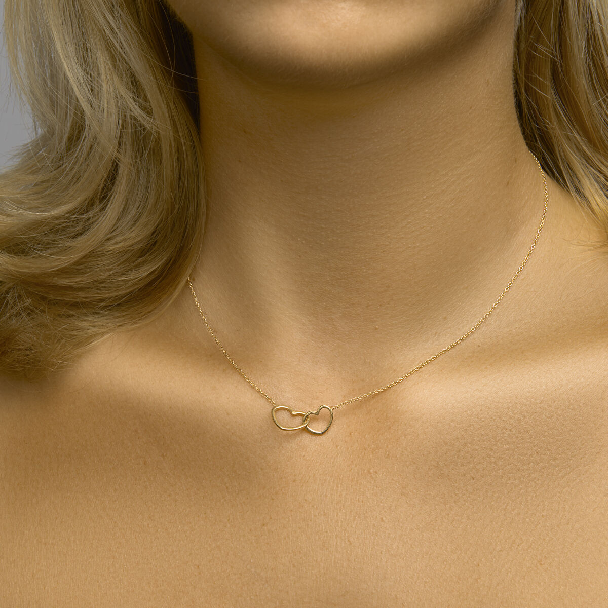 Een close-up van een vrouw met het Van der Kooij Collectie collier hartjes 40 + 5 cm 3 micron zilver verguld (geel), tegen een blote huid en blond haar - een elegant Valentijn cadeau.
