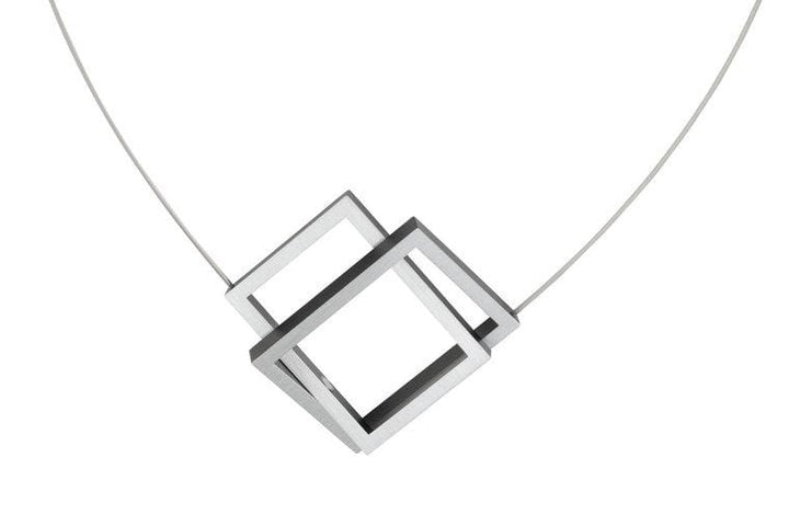 De Collier Twee rechthoeken in elkaar Zwart C30Z van CLIC Creations toont twee in elkaar grijpende zilveren vierkante frames in een hoek op een dunne draad. Met een magnetische sluiting combineert het moderne elegantie en bruikbaarheid tegen een effen witte achtergrond.