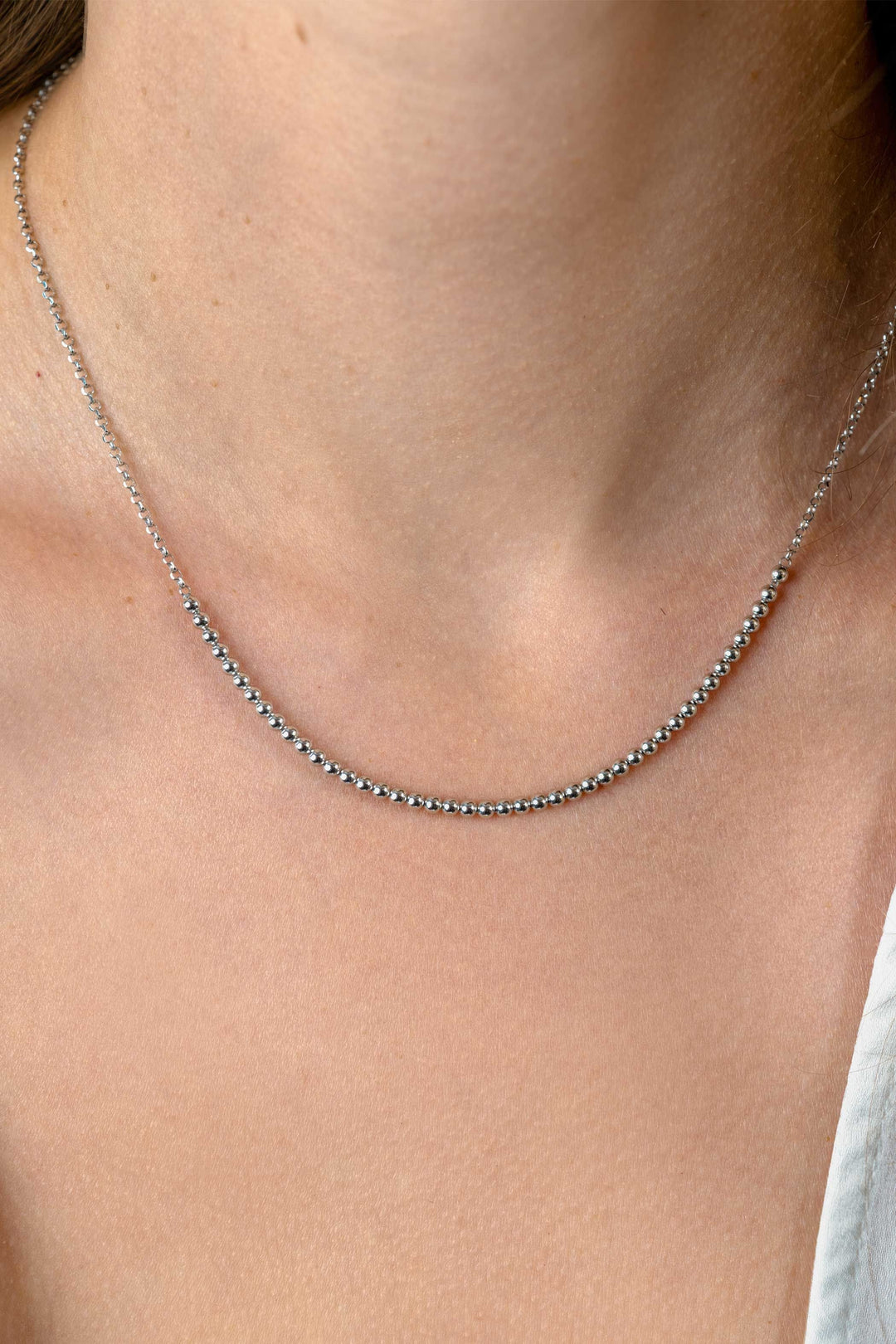 Een close-up van een hals die de Zinzi Ketting Zilver ZIC2640 van Zinzi draagt, met delicate zilveren kraaltjes, tegen een lichte huid. Rechtsonder is een wit topje zichtbaar.