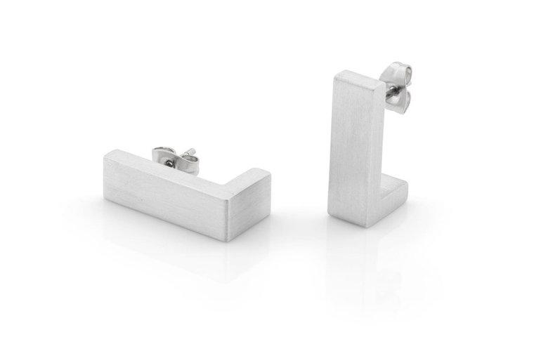 De CLIC Creations Oorsteker Om een hoekje O27 oorbellen, met een minimalistische geborstelde afwerking en rechthoekige vorm, worden getoond op een wit reflecterend oppervlak. Eén oorbel ligt plat, terwijl de andere rechtop staat, beide onthullen hun vlinderruggen en hypoallergene sluiting.