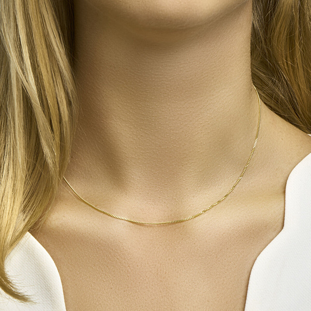 Een close-up van een vrouw met een lichte huid en blond haar in een witte top, waarbij haar nek benadrukt wordt, versierd met de Van der Kooij Collectie collier gourmette 4-zijdes geslepen 1,2 mm in 14K geelgoud.