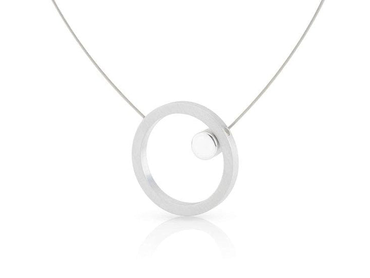 De Collier Grote ring met glans rondje C180 van CLIC Creations is een moderne, minimalistische ketting met een zilveren ronde hanger met een klein bolletje, opgehangen aan een delicate ketting. Handgemaakt in Nederland, het reflecteert subtiel licht en biedt een uniek maar eenvoudig ontwerp.