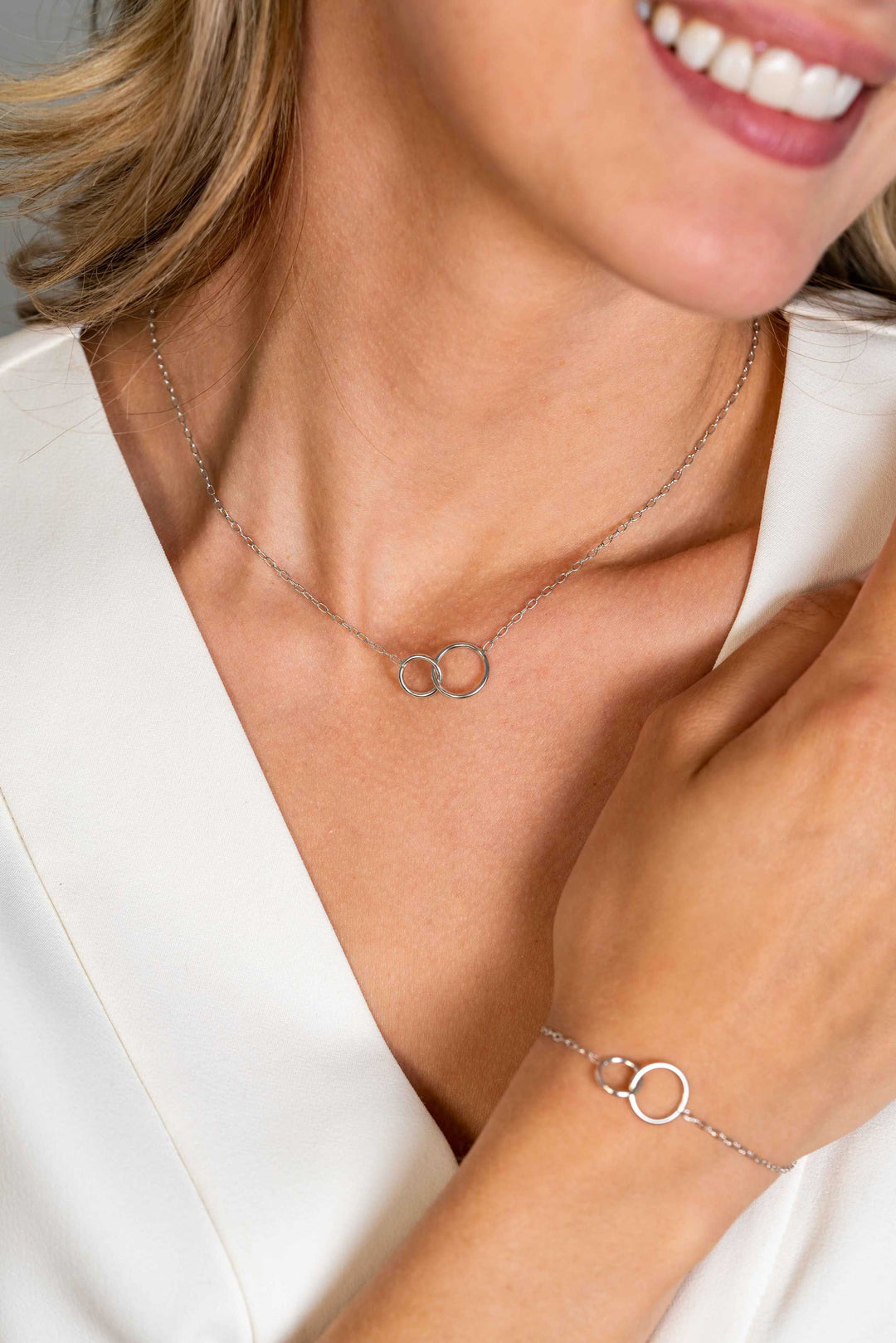 Een vrouw lacht in een wit topje en draagt de Zinzi Ketting Zilver Zic2275 ketting met in elkaar grijpende cirkels, die zachtjes haar sleutelbeen raakt.