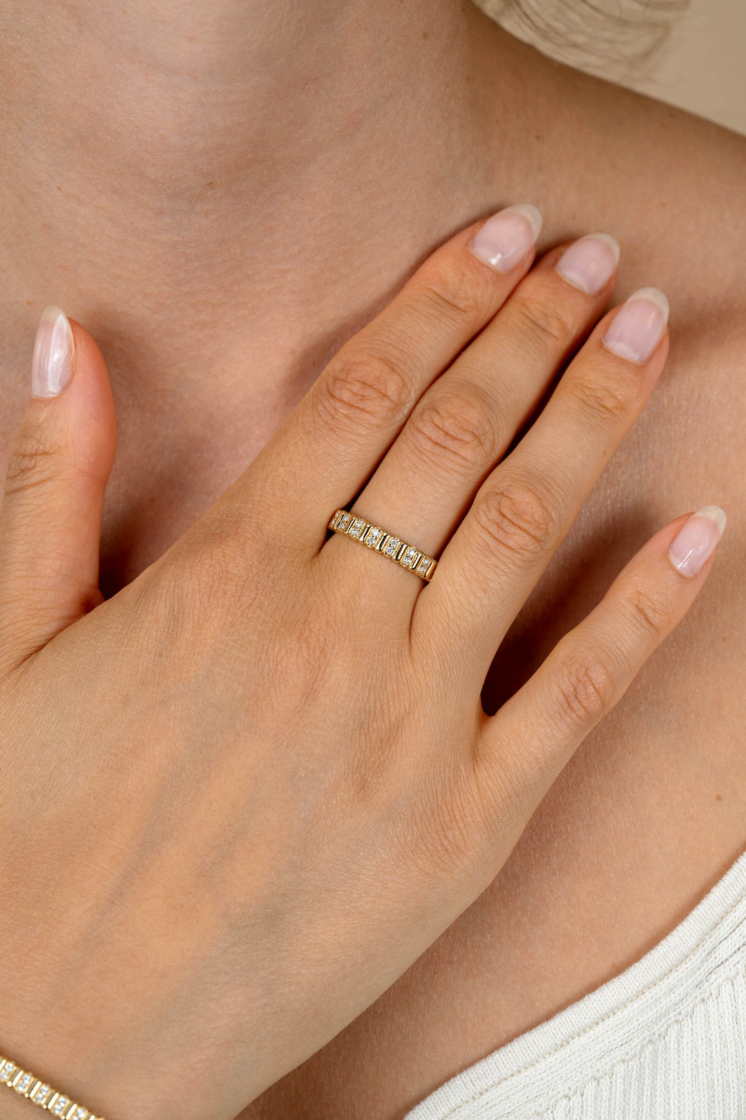 Een close-up van een hand met gemanicuurde nagels die de Zinzi Ring Zilver ZIR2686Y van Zinzi draagt, met vierkant geslepen stenen, aan de ringvinger, zachtjes rustend op de borst. De persoon is gekleed in een wit topje met structuur.