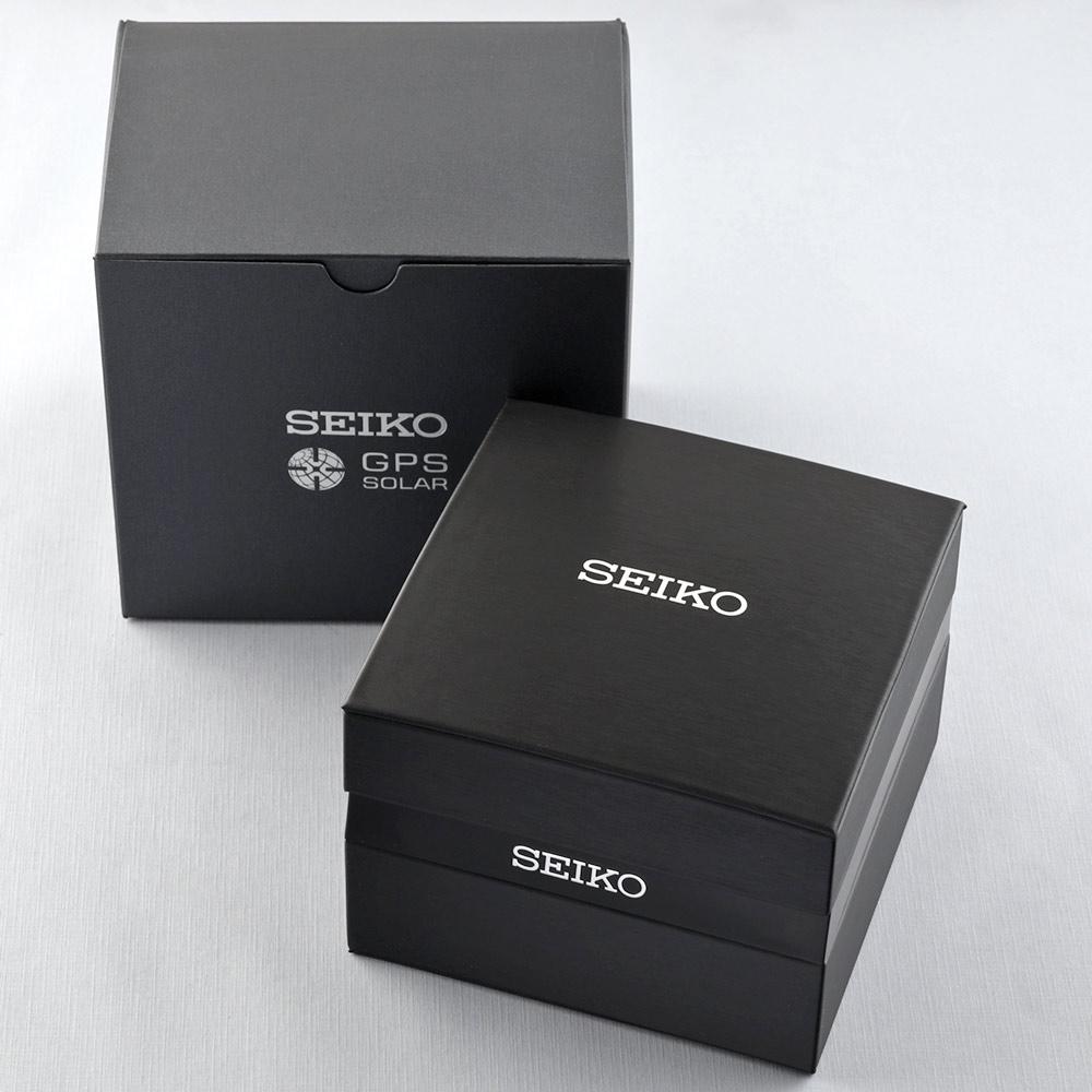 Er worden twee zwarte dozen getoond: een grotere Seiko GPS Solar en een kleinere glanzende Seiko, beide op een lichtgrijs oppervlak. Ze hinten naar het precisievakmanschap van de Seiko Astron herenhorloge SSJ015J1 binnenin, aangestuurd door zonne-energie.