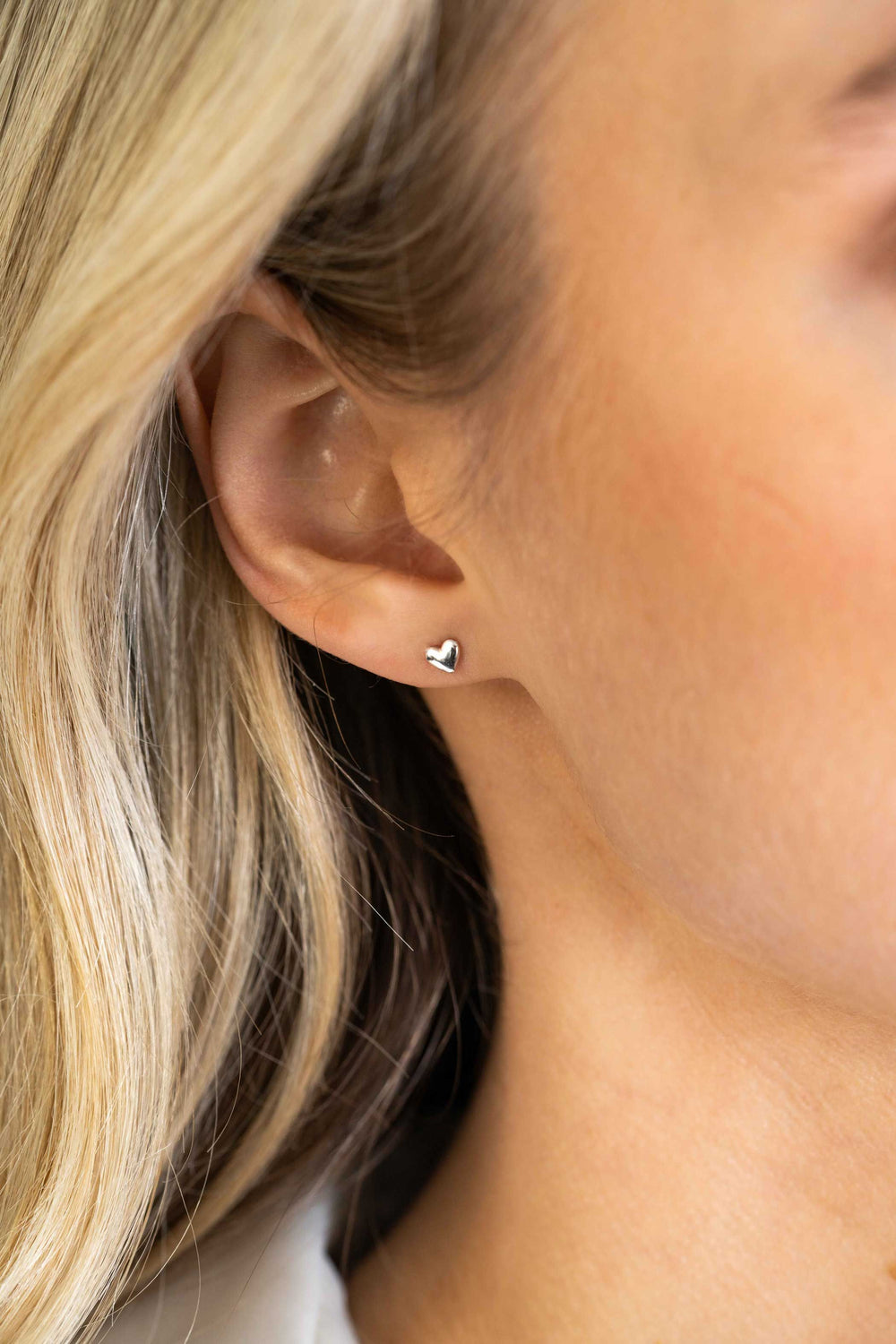 Close-up van het oor van een persoon met steil blond haar, die elegante Zinzi Oorbellen Zilver Zio2365 oorbellen draagt. De achtergrond is onscherp, waardoor het glanzende zilveren ontwerp en de kenmerkende stijl van het merk worden benadrukt.